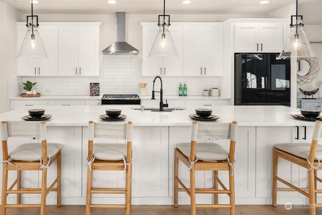 kitchen featuring sink, a breakfast bar area, range, black fridge, and wall chimney range hood