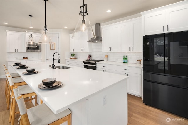 kitchen with sink, wall chimney range hood, white cabinets, and appliances with stainless steel finishes