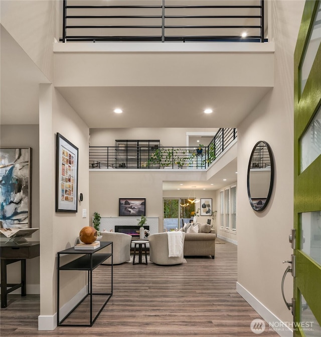 interior space featuring recessed lighting, a high ceiling, wood finished floors, baseboards, and a glass covered fireplace