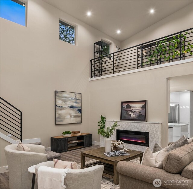 living area featuring a glass covered fireplace, a towering ceiling, wood finished floors, stairs, and recessed lighting