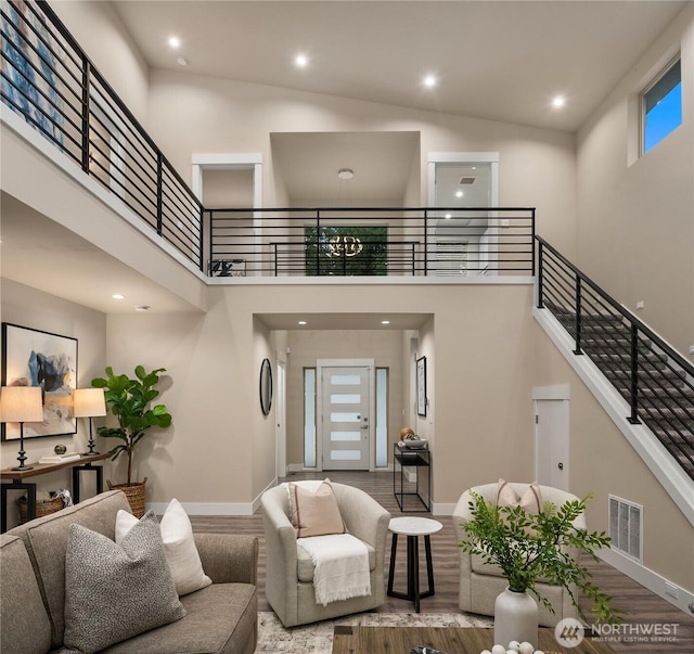 living room featuring wood finished floors, a towering ceiling, visible vents, stairs, and baseboards