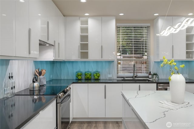 kitchen with dark stone counters, stainless steel range with electric cooktop, white cabinetry, open shelves, and a sink