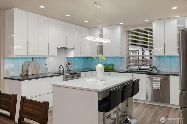 kitchen featuring a center island, light wood finished floors, appliances with stainless steel finishes, white cabinetry, and a sink