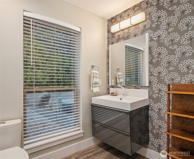 bathroom with toilet, vanity, wood finished floors, baseboards, and wallpapered walls