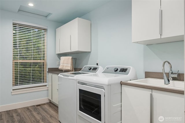 washroom featuring cabinet space, baseboards, dark wood-type flooring, washing machine and clothes dryer, and a sink