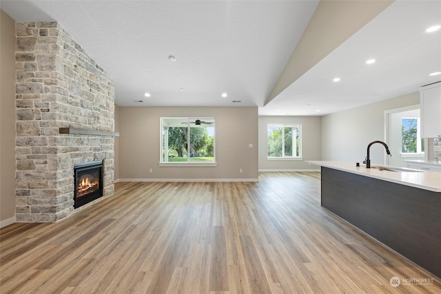 unfurnished living room with lofted ceiling, a fireplace, light hardwood / wood-style floors, and sink