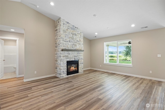 unfurnished living room with lofted ceiling, a stone fireplace, and light hardwood / wood-style flooring