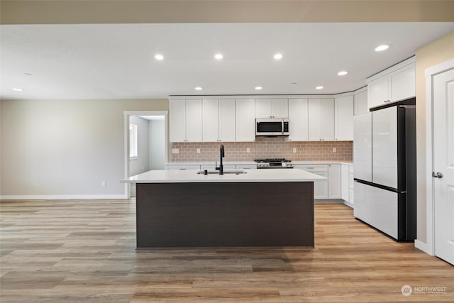 kitchen with stainless steel appliances, an island with sink, sink, and white cabinets