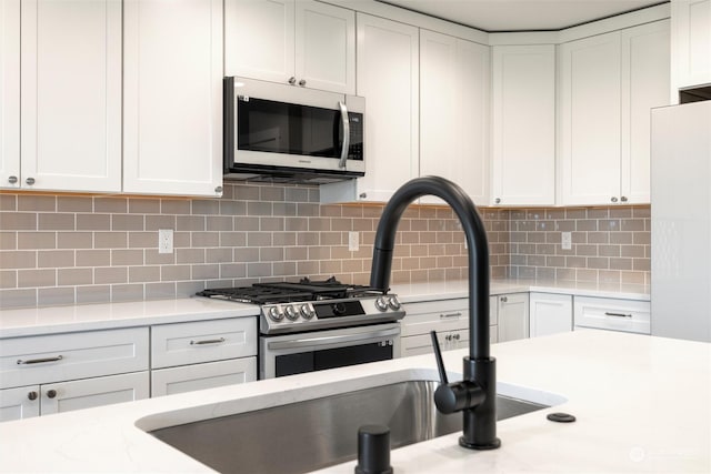 kitchen with tasteful backsplash, white cabinetry, appliances with stainless steel finishes, and light stone countertops