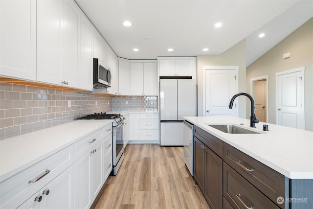 kitchen featuring sink, appliances with stainless steel finishes, white cabinetry, light hardwood / wood-style floors, and a center island with sink