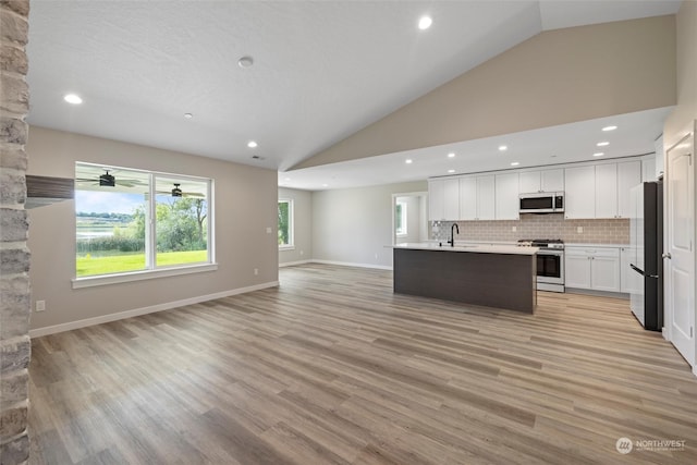 kitchen featuring light hardwood / wood-style flooring, white cabinetry, backsplash, stainless steel appliances, and a center island with sink