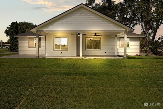 back house at dusk featuring ceiling fan, a patio area, and a lawn