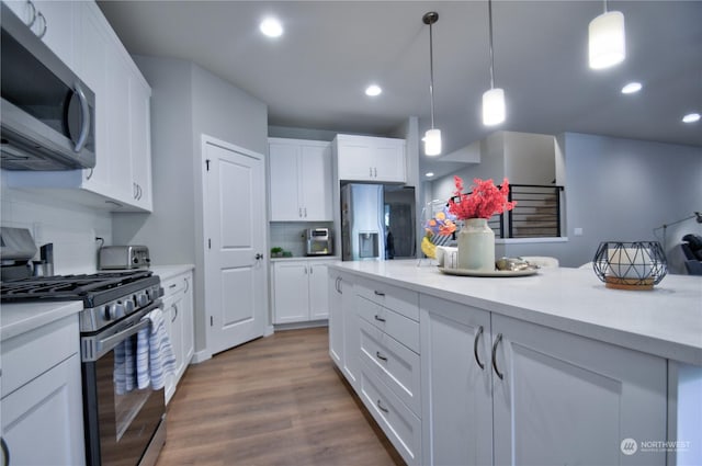 kitchen with white cabinetry, wood-type flooring, hanging light fixtures, appliances with stainless steel finishes, and decorative backsplash