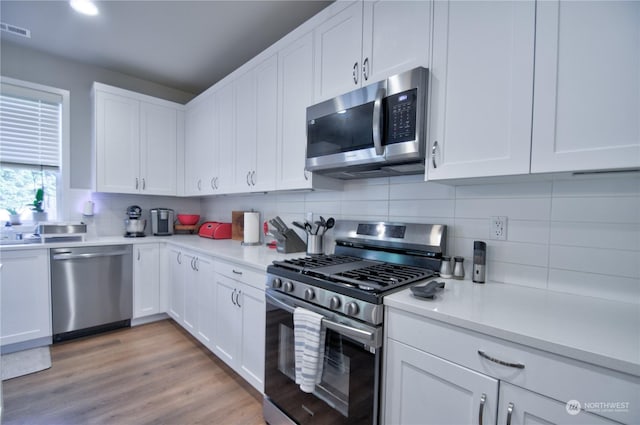 kitchen with stainless steel appliances, white cabinetry, light hardwood / wood-style flooring, and decorative backsplash