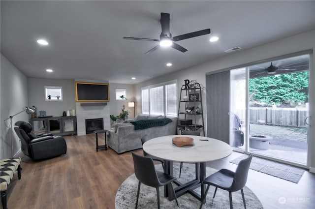 dining room with wood-type flooring, ceiling fan, and a fireplace