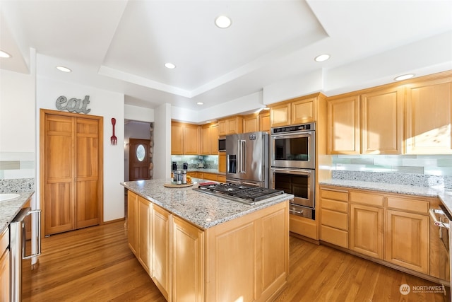 kitchen with appliances with stainless steel finishes, decorative backsplash, a center island, light stone counters, and light hardwood / wood-style flooring