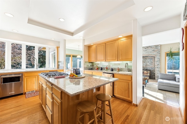 kitchen featuring sink, a center island, light wood-type flooring, appliances with stainless steel finishes, and a raised ceiling