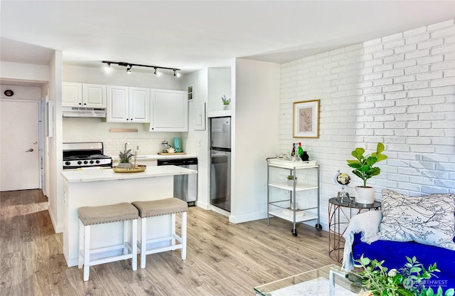 kitchen with light hardwood / wood-style flooring, appliances with stainless steel finishes, a kitchen breakfast bar, tasteful backsplash, and white cabinets