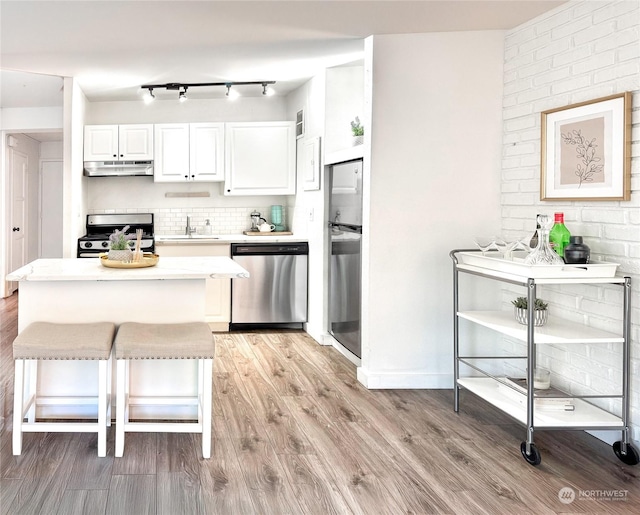 kitchen with appliances with stainless steel finishes, white cabinetry, sink, a breakfast bar area, and light hardwood / wood-style floors