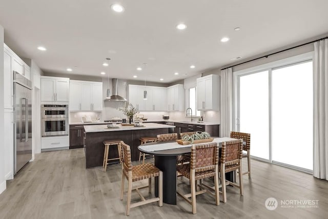 kitchen featuring wall chimney range hood, a breakfast bar, stainless steel appliances, white cabinets, and a kitchen island