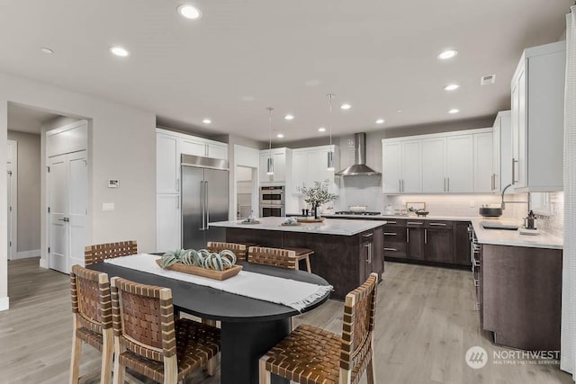 kitchen with a kitchen bar, sink, a center island, stainless steel appliances, and wall chimney range hood