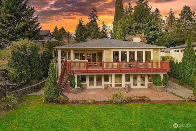 back house at dusk featuring french doors, a deck, a patio area, and a lawn