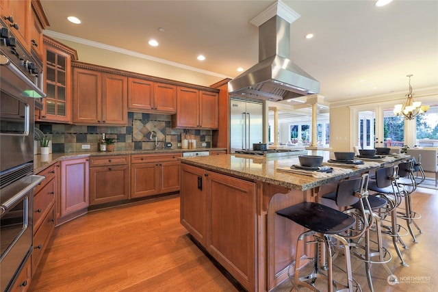 kitchen featuring pendant lighting, a kitchen breakfast bar, light stone counters, island range hood, and a kitchen island