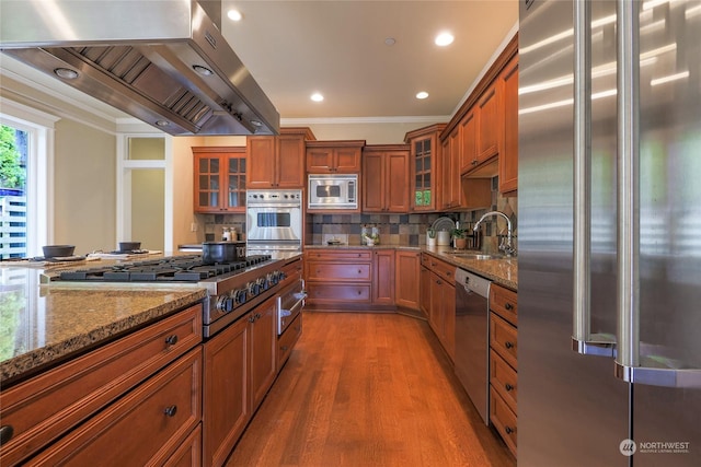 kitchen with tasteful backsplash, wood-type flooring, stainless steel appliances, light stone countertops, and exhaust hood