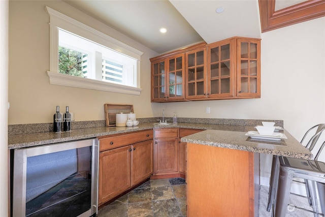 kitchen featuring sink, a breakfast bar, light stone counters, kitchen peninsula, and beverage cooler