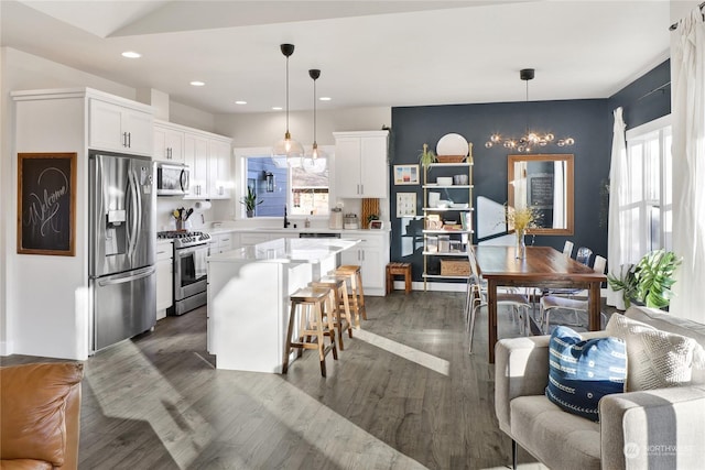 kitchen with a kitchen island, appliances with stainless steel finishes, white cabinetry, a kitchen breakfast bar, and hanging light fixtures