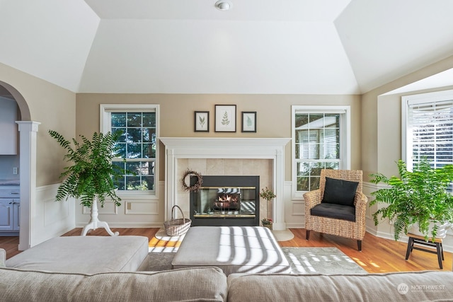 living room with vaulted ceiling, wood finished floors, arched walkways, and a tile fireplace