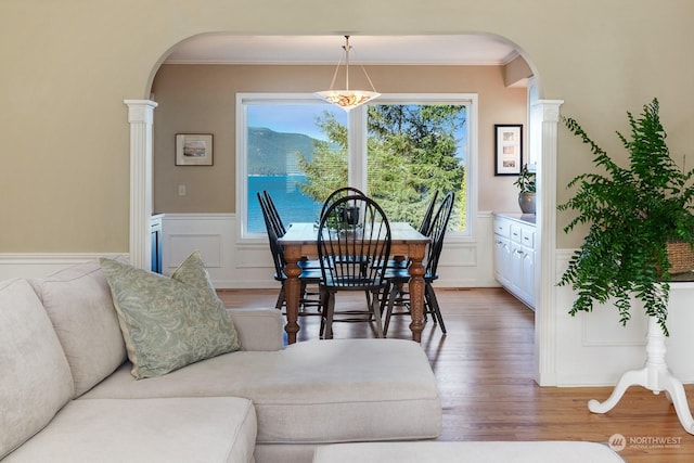 dining space with light wood finished floors, arched walkways, and ornamental molding