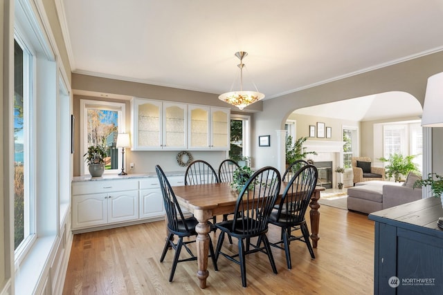 dining room with light wood-style floors, arched walkways, ornamental molding, and a glass covered fireplace