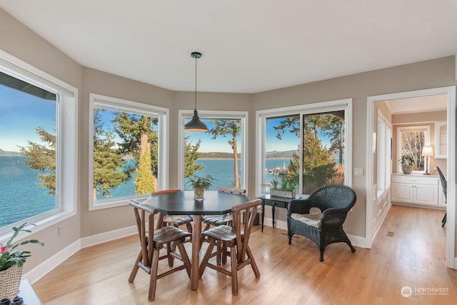 dining space featuring light wood-type flooring, a water view, and baseboards