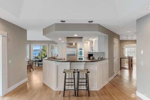 kitchen with appliances with stainless steel finishes, a peninsula, a sink, white cabinetry, and backsplash