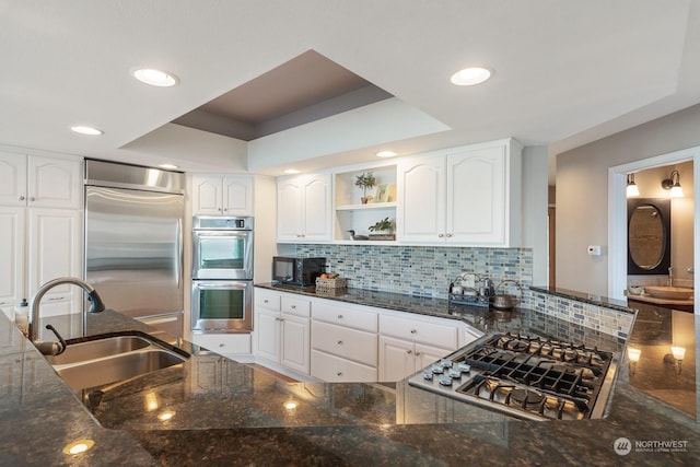 kitchen with stainless steel appliances, tasteful backsplash, white cabinetry, a sink, and dark stone countertops