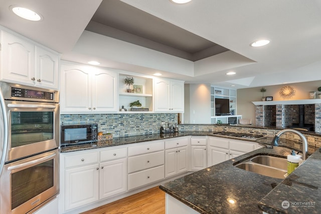 kitchen featuring a raised ceiling, decorative backsplash, appliances with stainless steel finishes, a sink, and dark stone countertops