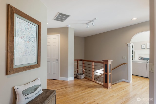 hallway featuring light wood finished floors, visible vents, arched walkways, and an upstairs landing