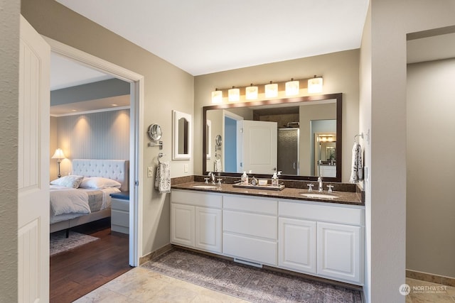 bathroom featuring double vanity, a stall shower, a sink, and baseboards