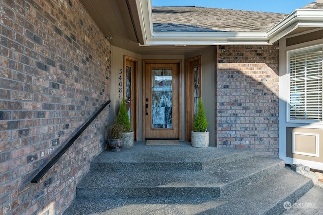 property entrance featuring brick siding and roof with shingles