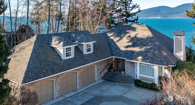 view of front of house featuring a garage, a water and mountain view, and roof with shingles