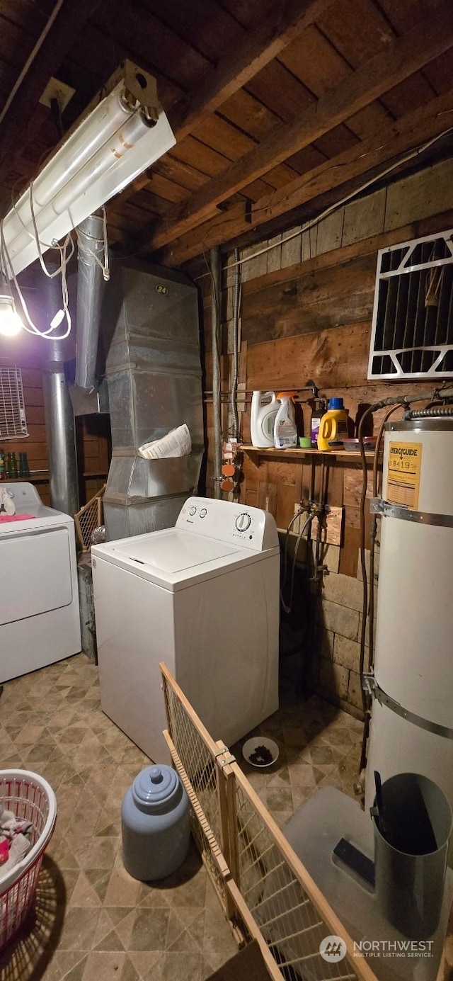 washroom featuring secured water heater, washing machine and dryer, and wood walls