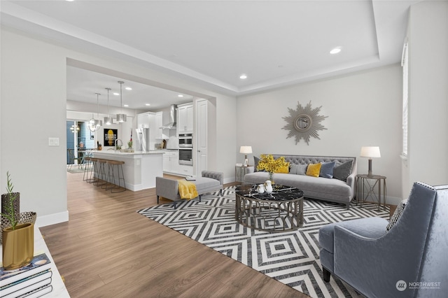 living room with sink, hardwood / wood-style floors, an inviting chandelier, and a tray ceiling