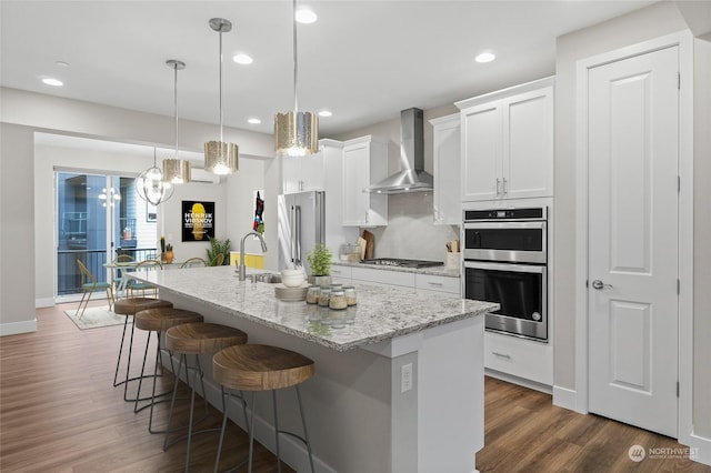 kitchen featuring wall chimney range hood, an island with sink, and white cabinets