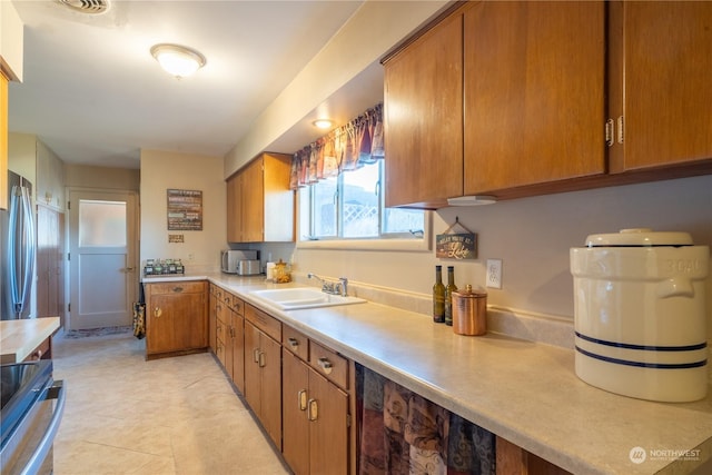 kitchen featuring light countertops, electric range, brown cabinetry, a sink, and stainless steel fridge