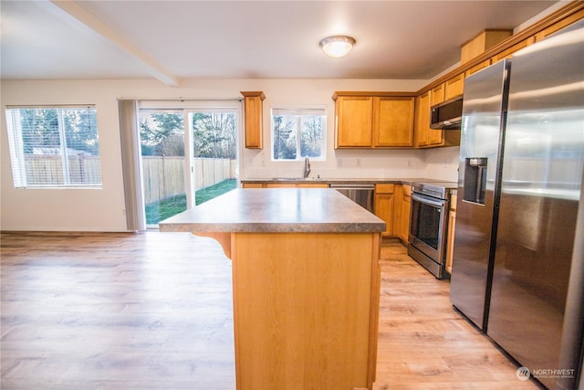 kitchen with sink, a center island, light wood-type flooring, appliances with stainless steel finishes, and a kitchen breakfast bar