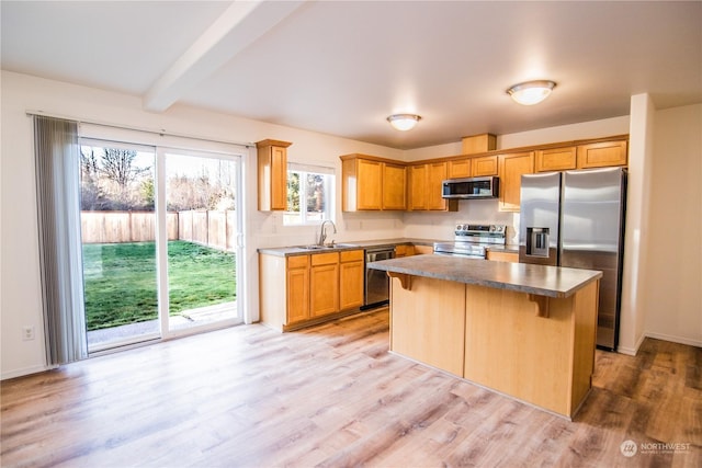 kitchen with appliances with stainless steel finishes, sink, light wood-type flooring, a center island, and beam ceiling