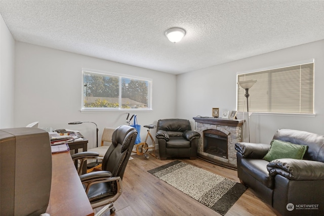 office space with a stone fireplace, a textured ceiling, and light wood-type flooring