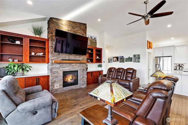 living room featuring a fireplace, vaulted ceiling, ceiling fan, and light wood-type flooring