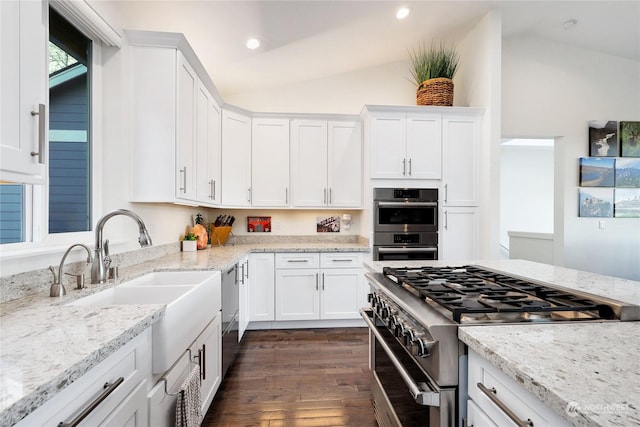 kitchen featuring lofted ceiling, light stone countertops, white cabinets, and appliances with stainless steel finishes